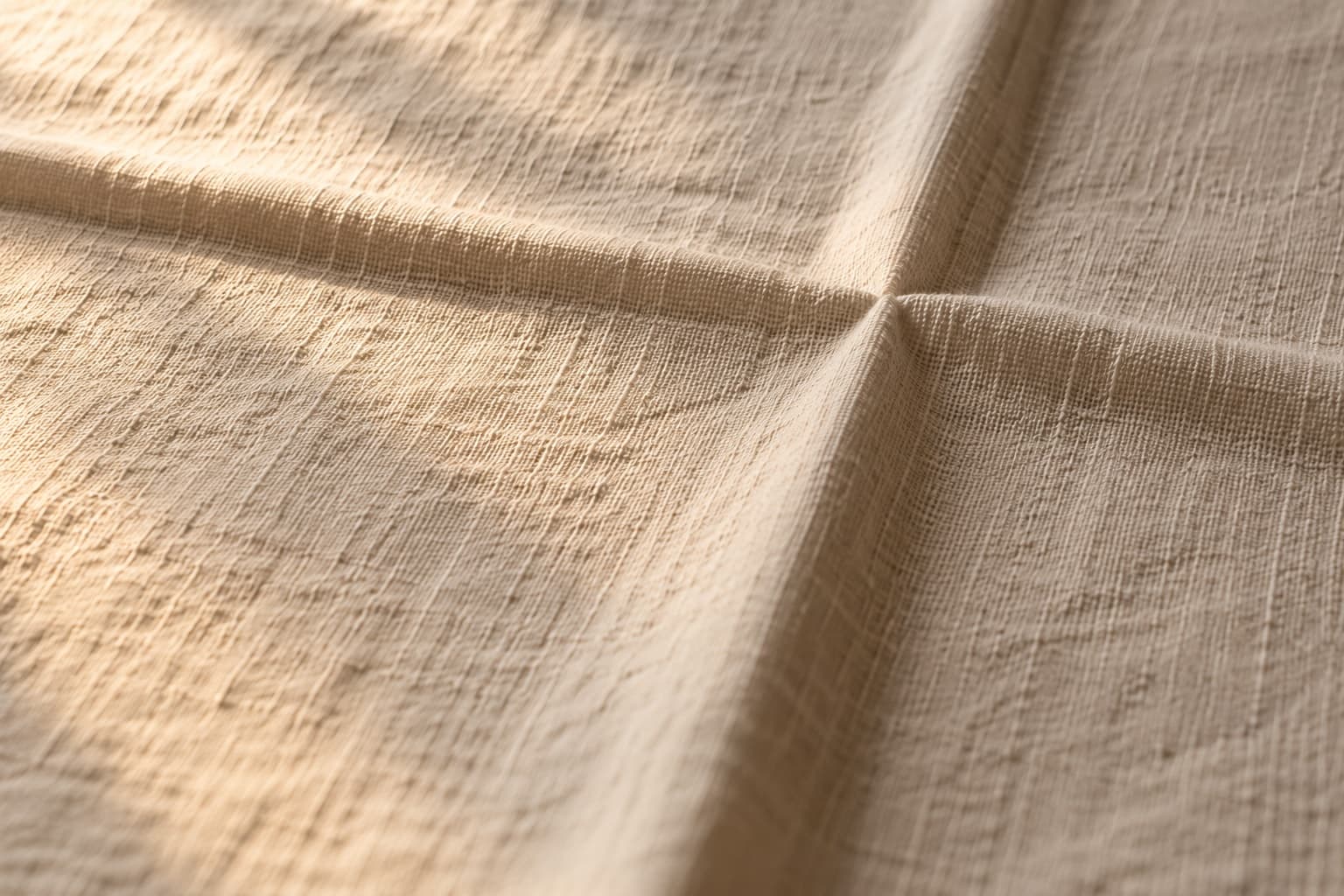 Close on a linen cloth where two creases meet, the fold reading as a cross